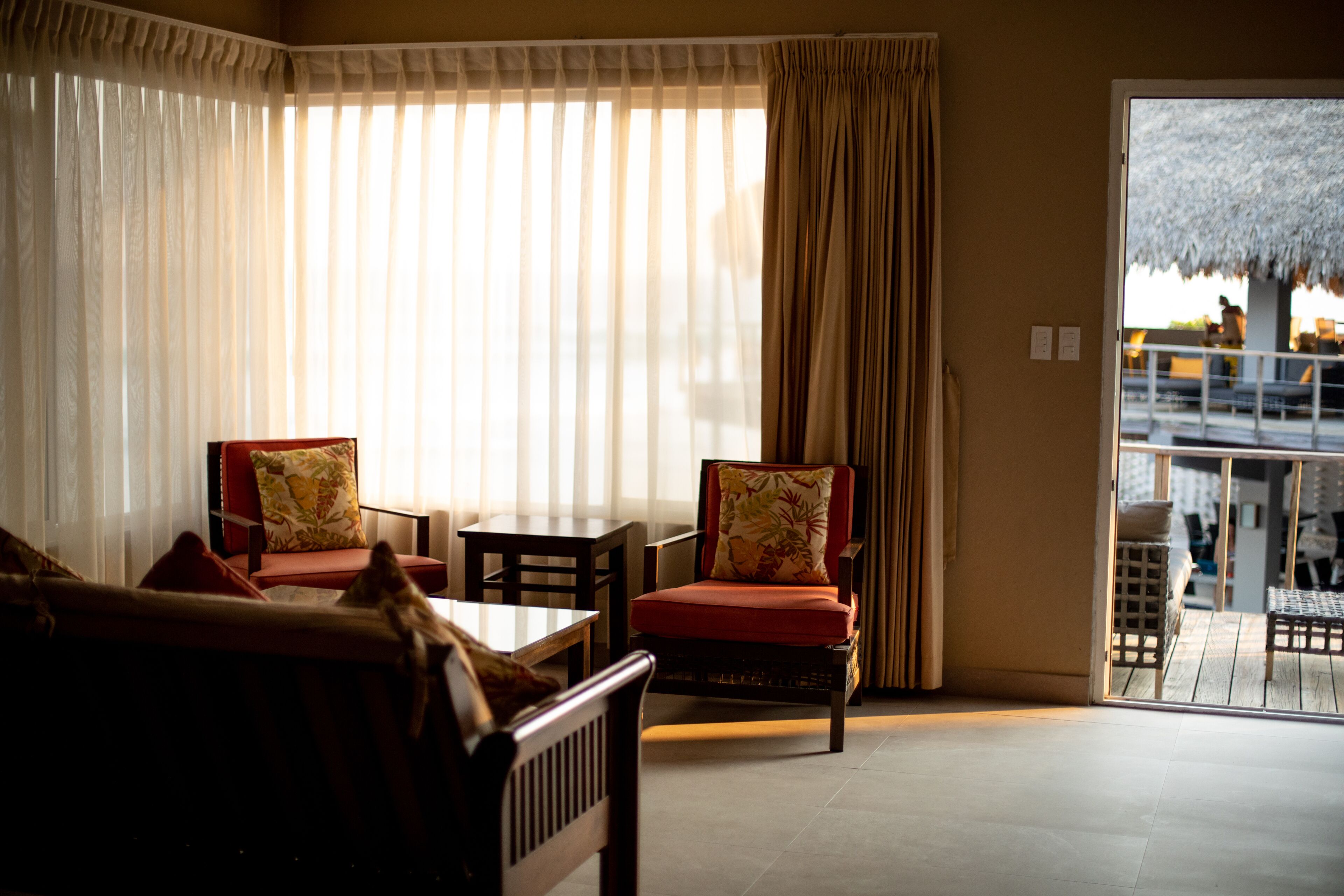 A room with a sofa, two armchairs, a table, and a view of a balcony with outdoor furniture.