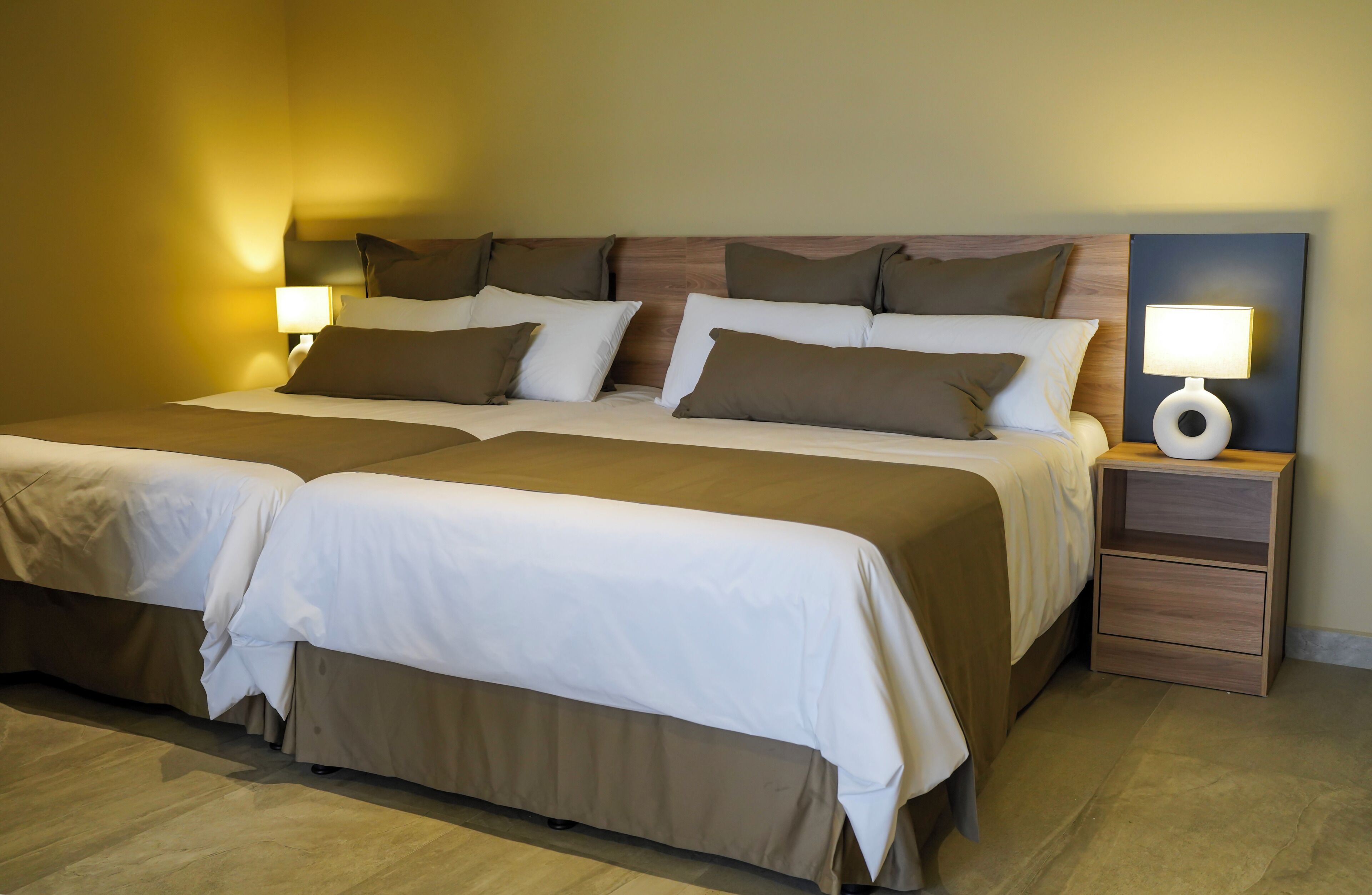 A double bed with two bedside tables, each with a lamp, in a room with wooden flooring and a neutral color scheme.
