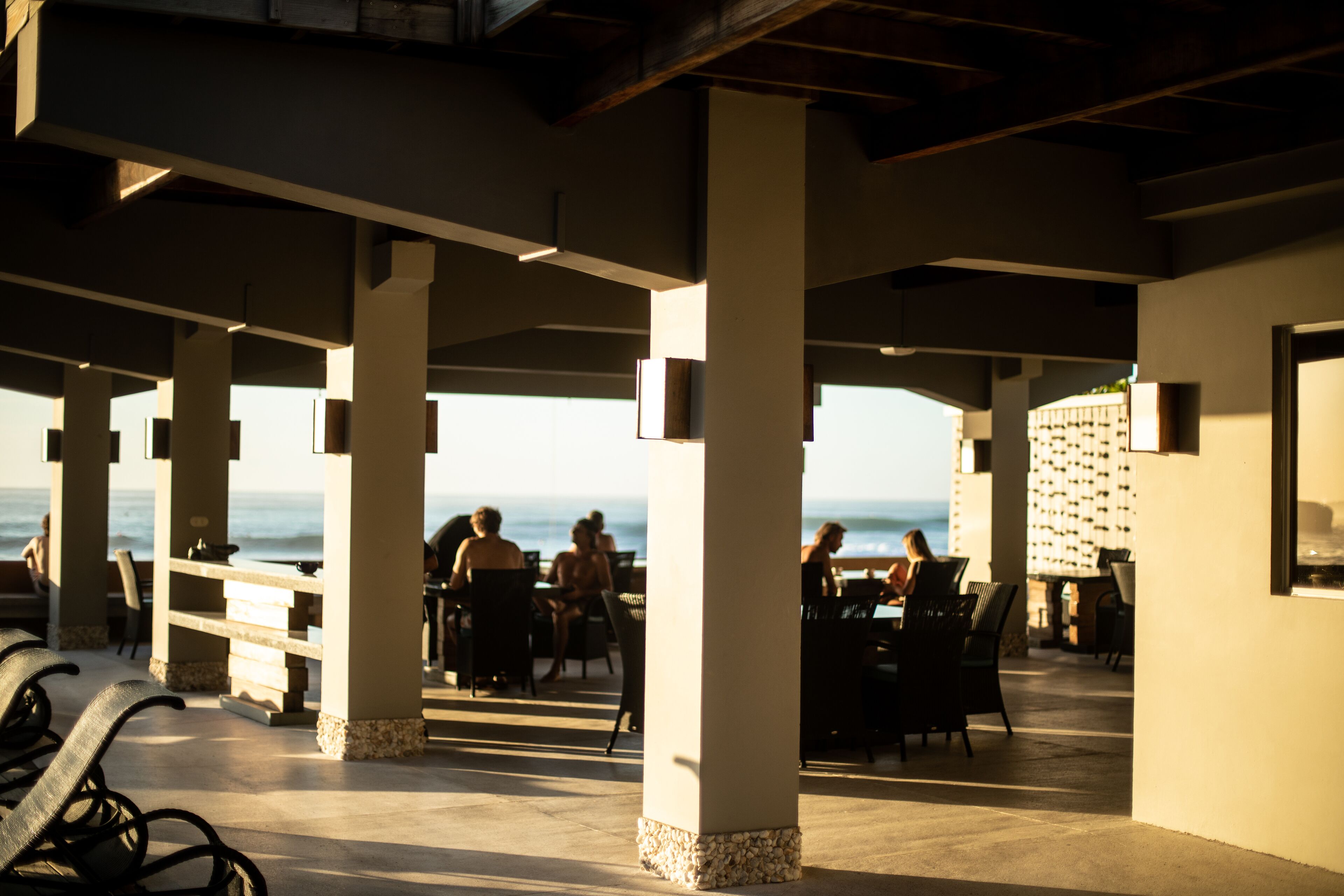 An outdoor seating area with tables and chairs, large pillars, and a view of the ocean.