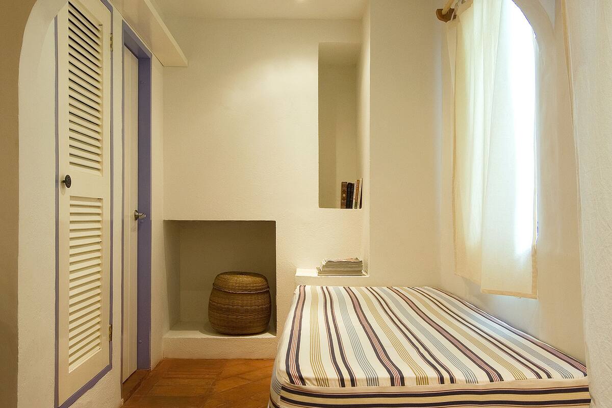 Une chambre à coucher avec un lit, une petite fenêtre, un miroir et une porte.