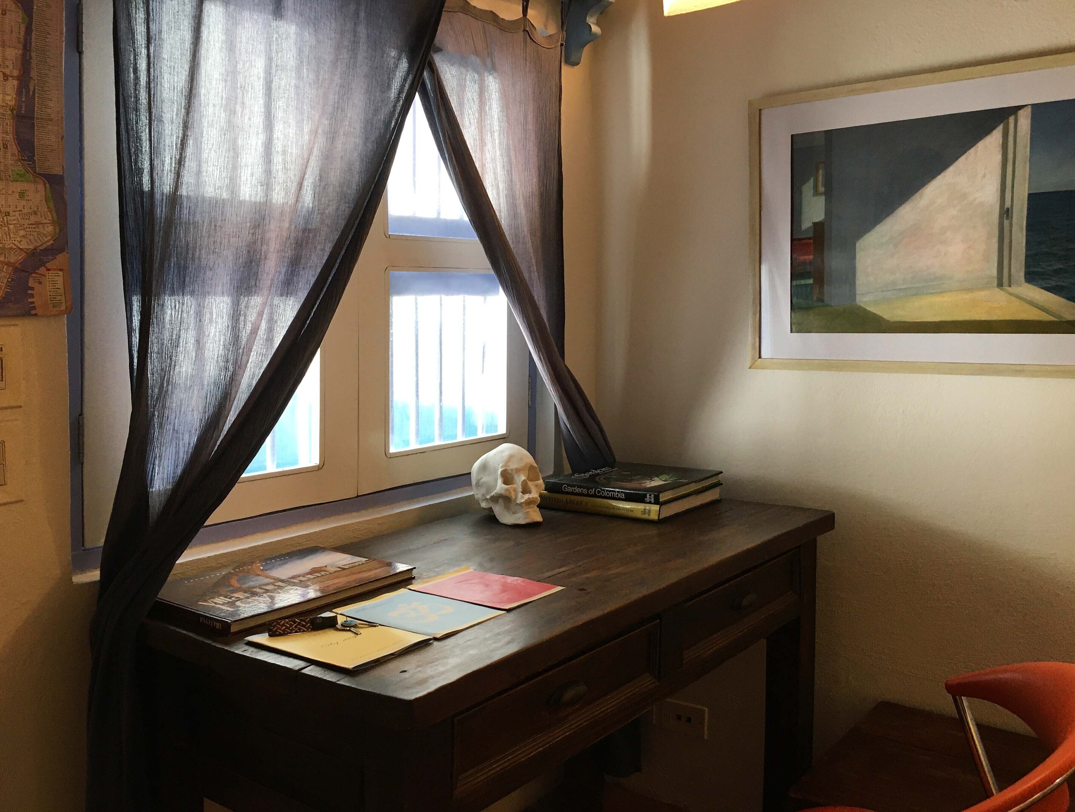Un salón de estudio con un escritorio, un cráneo, libros y un cuadro en la pared.