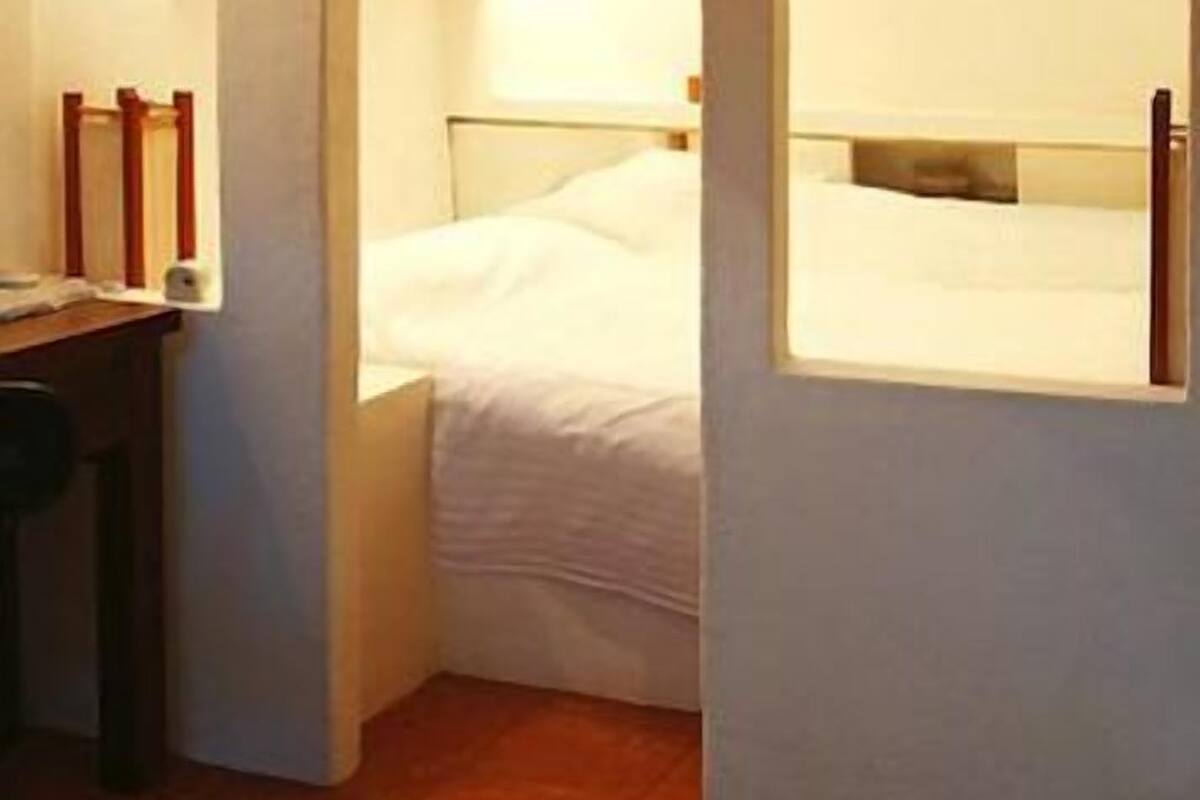 Une petite chambre à coucher accueillante, avec un lit simple, un bureau et une chaise. Trois fenêtres en arc donnent sur la pièce et laissent entrer la lumière naturelle.