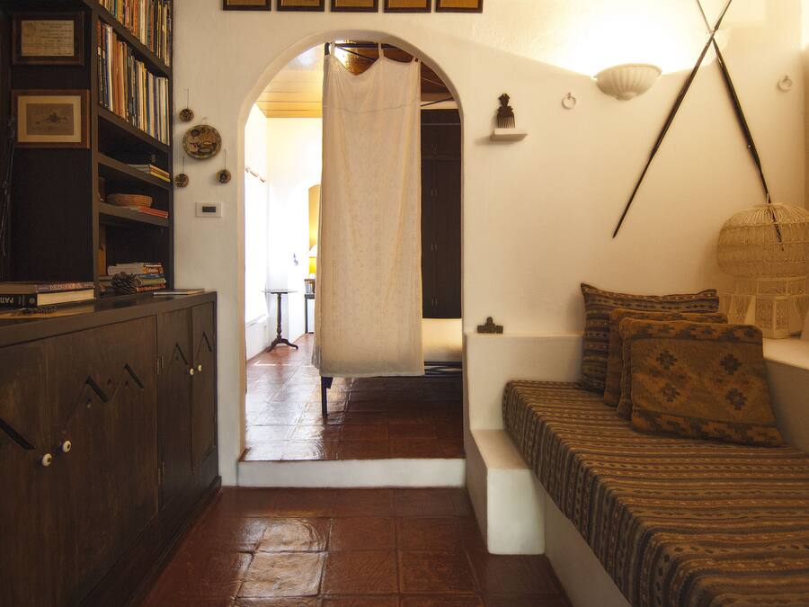 Um quarto com um armário de madeira, um sofá estampado, um candeeiro pendente e uma estante repleta de livros.