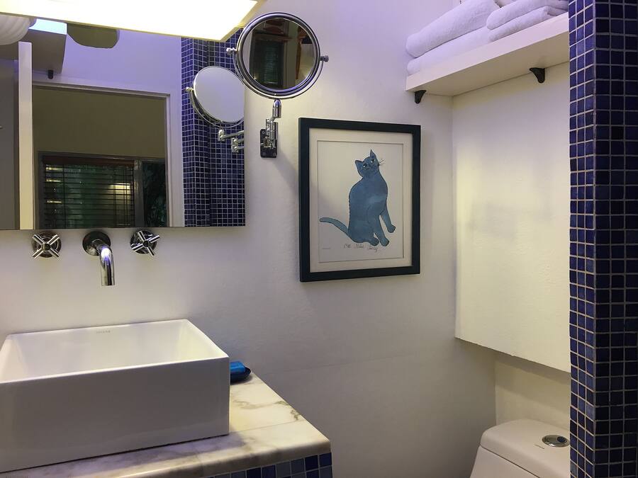 A bathroom with a white sink, a framed cat illustration, a mirror, and a toilet.