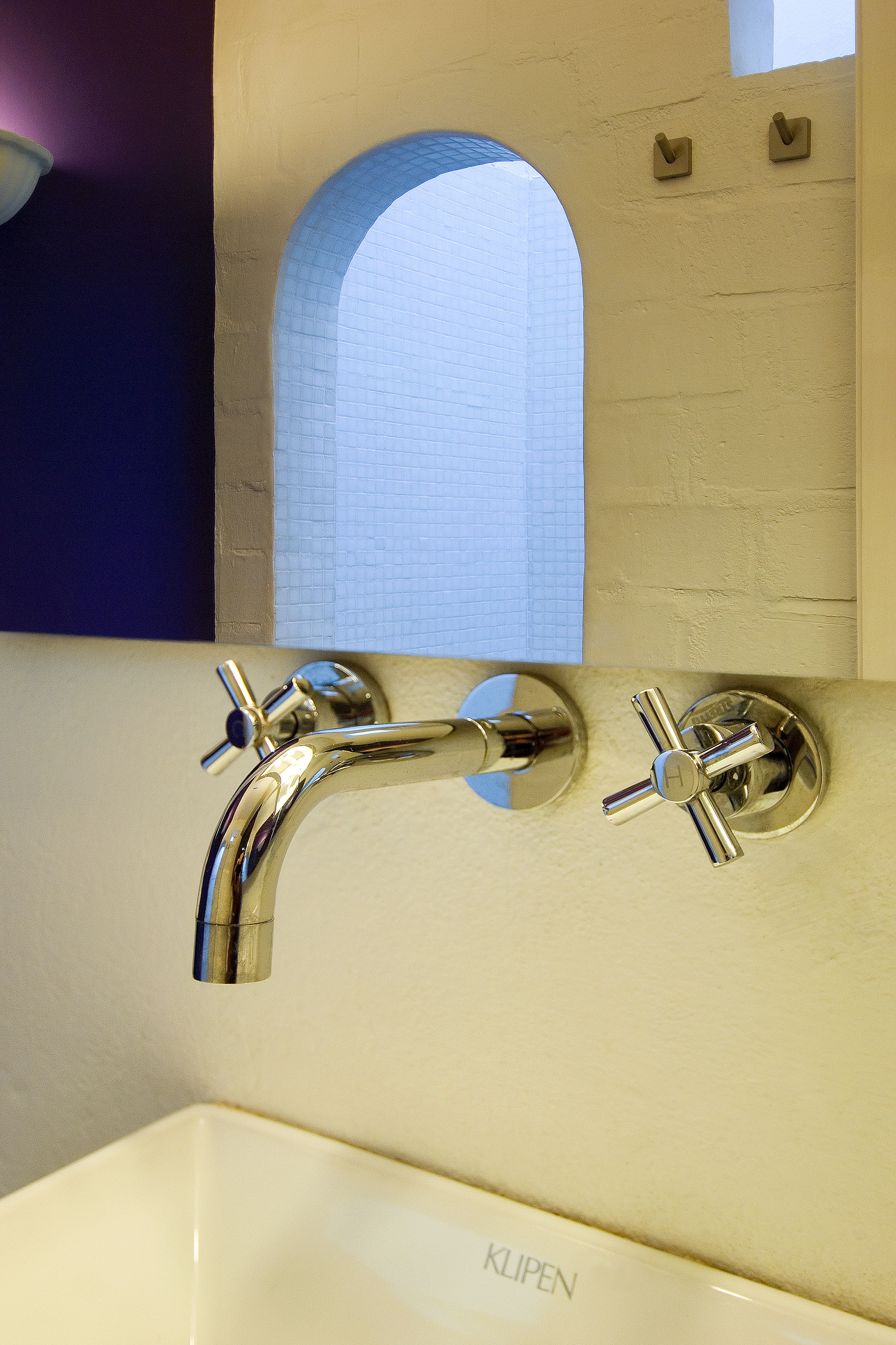 A bathroom with a white sink, chrome faucets, and a tiled wall.