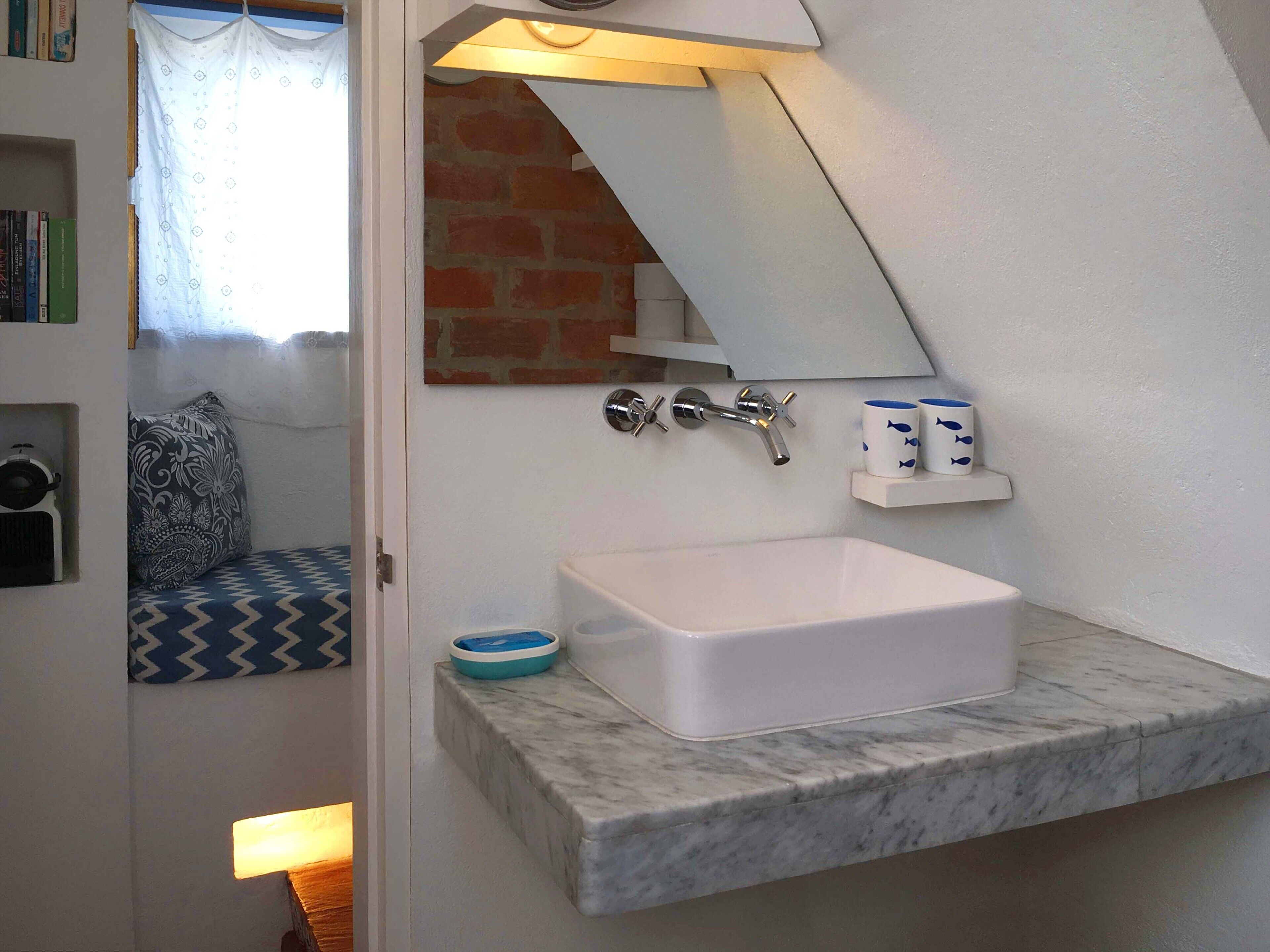 A bathroom with a white sink, a mirror, and a shelf with toiletries.