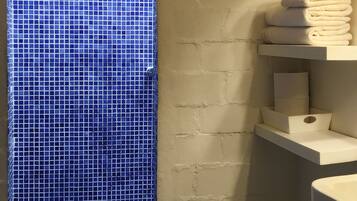 A bathroom with a tiled wall, a window, and a stack of towels on a shelf.