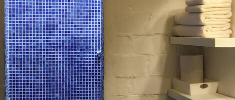 A bathroom with a tiled wall, a window, and a stack of towels on a shelf.