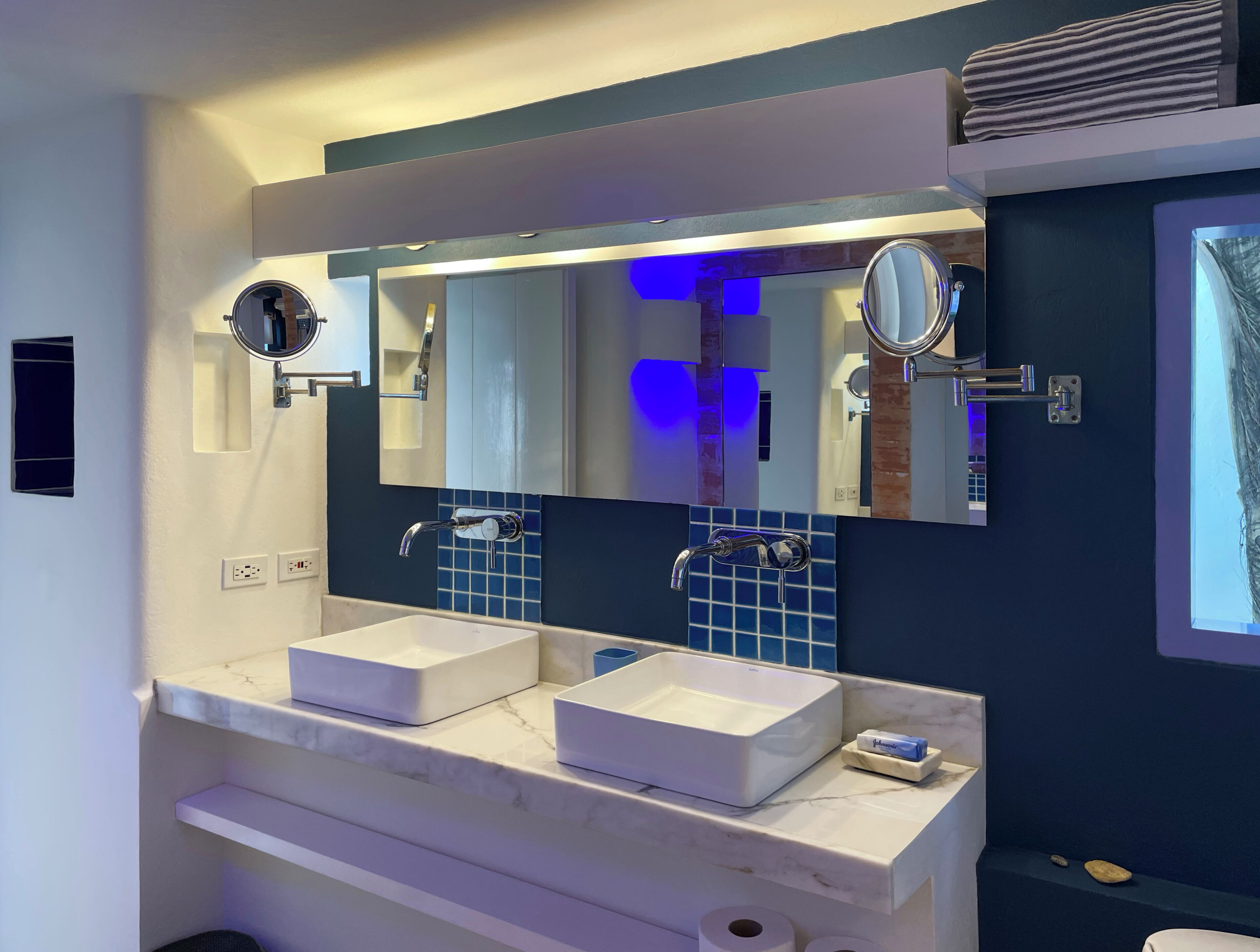 A modern bathroom with two white sinks, a large mirror, and a blue-tiled backsplash.