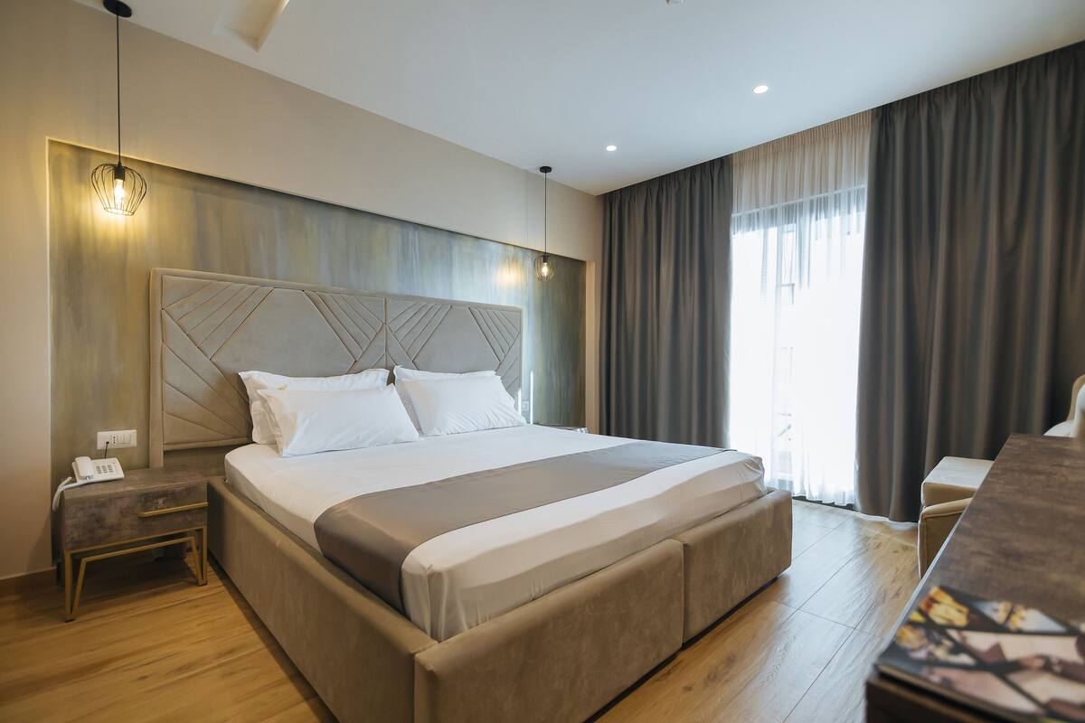 A modern hotel room with a large bed, a bedside table with a phone, and a desk with a chair.