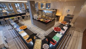 A buffet setup with various food items and a central display case, surrounded by seating areas. - Brilliant Hotel & Spa (Golem)