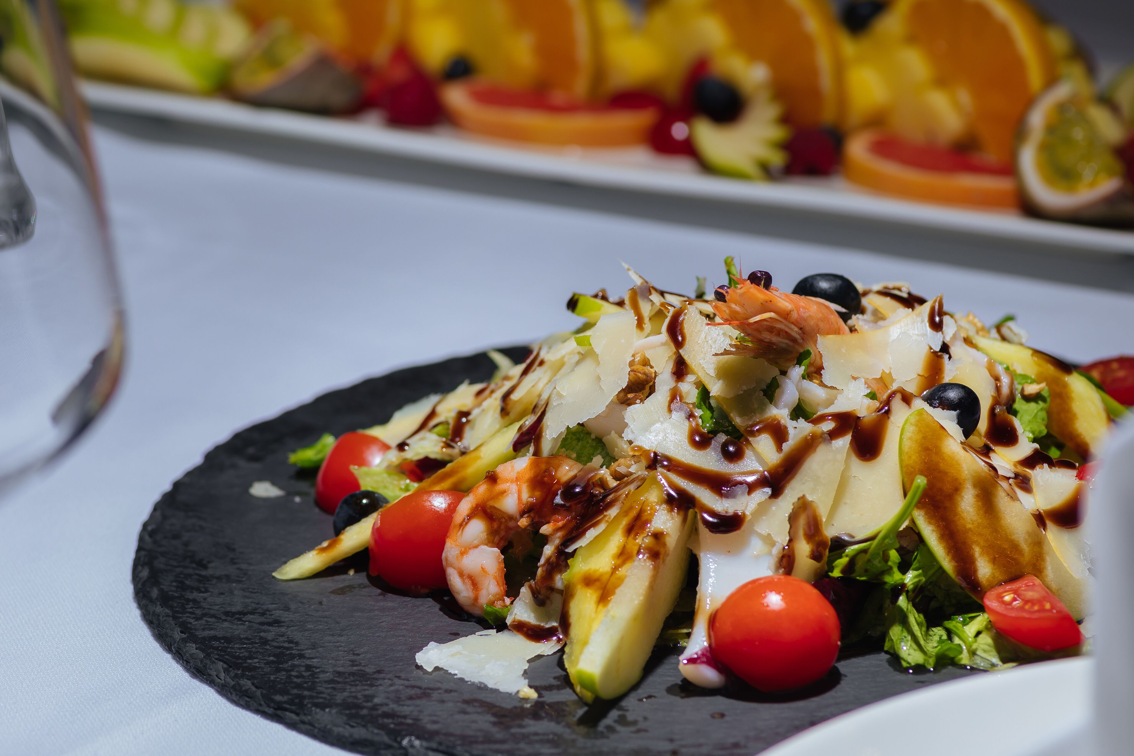 Primer plano de una ensalada gourmet con diversos ingredientes y un chorrito de salsa, servida en un plato negro.