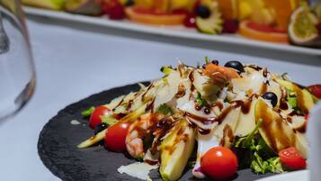 Primer plano de una ensalada gourmet con diversos ingredientes y un chorrito de salsa, servida en un plato negro.