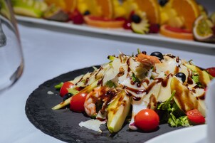 Primer plano de una ensalada gourmet con diversos ingredientes y un chorrito de salsa, servida en un plato negro.