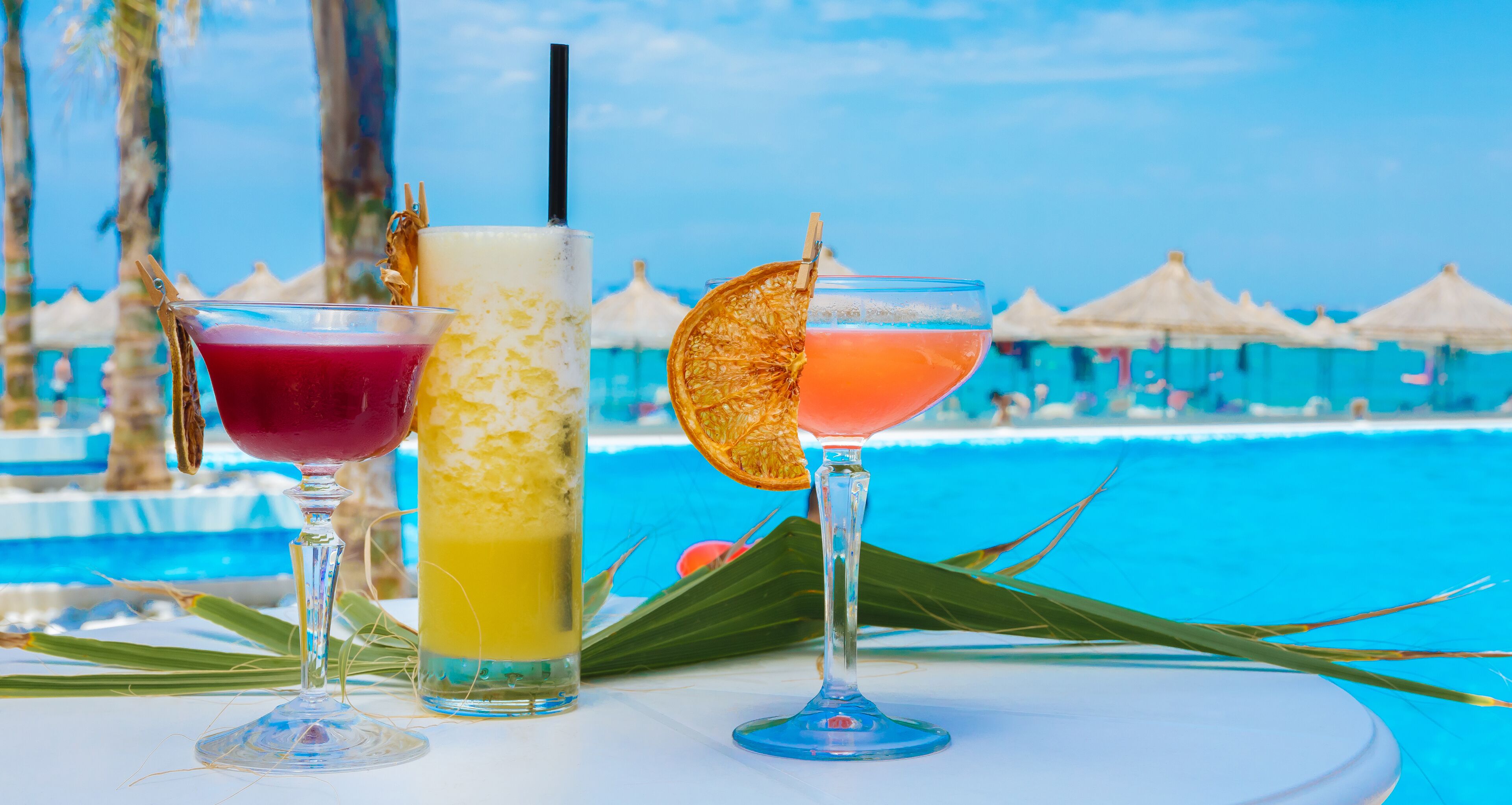 Tre cocktail su un tavolo vicino a una piscina, con ombrelloni sullo sfondo.