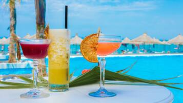 Tre cocktail su un tavolo vicino a una piscina, con ombrelloni sullo sfondo.