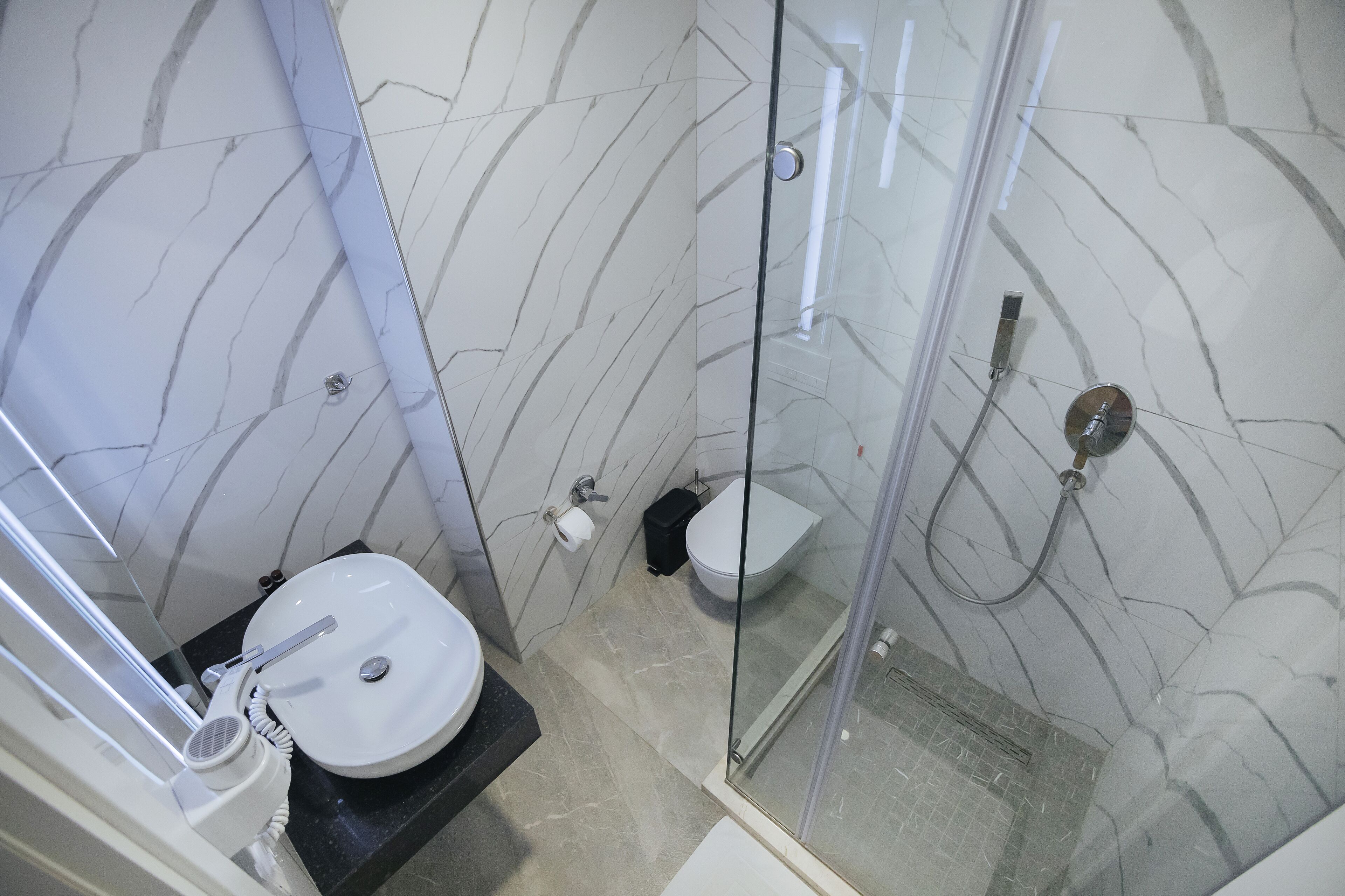 Ein modernes Badezimmer mit einer gläsernen Duschkabine, einem weißen Waschbecken und einer Toilette.