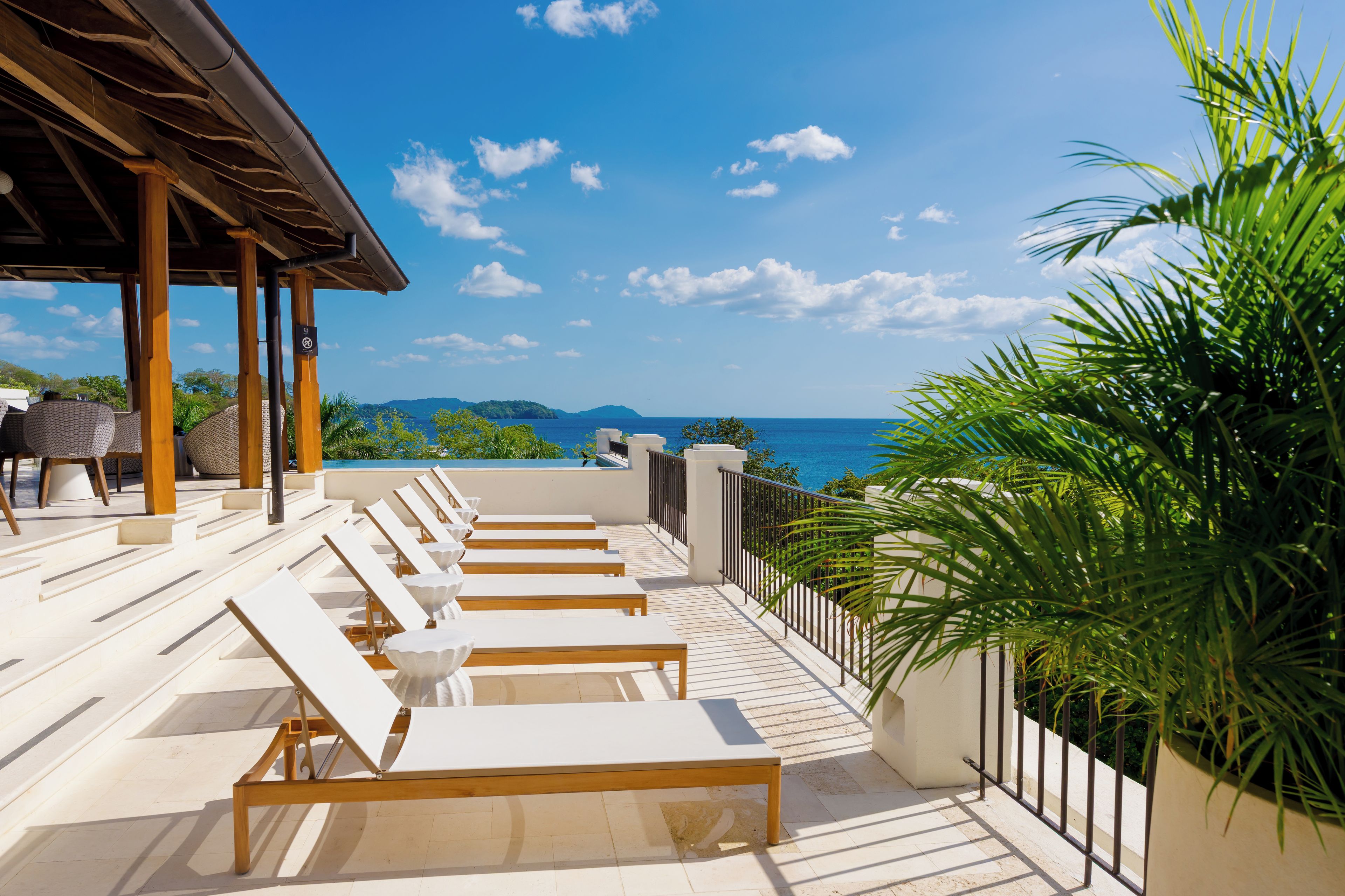 Une terrasse avec des chaises longues, une piscine et une vue sur la mer.