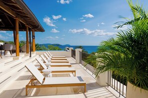 Una terraza con sillones de sol, una piscina y vistas al mar.
