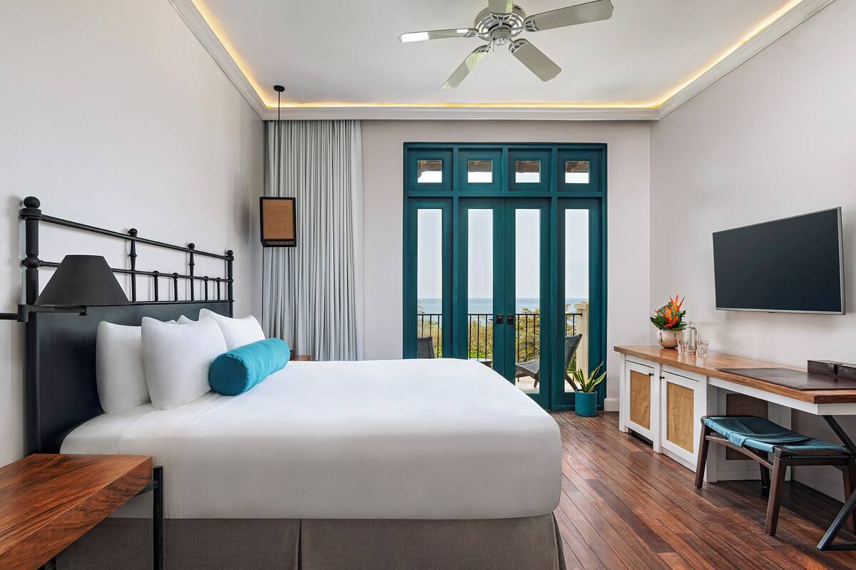 Habitació d'hotel moderna amb llit, escriptori, televisió i un balcó amb vistes.
