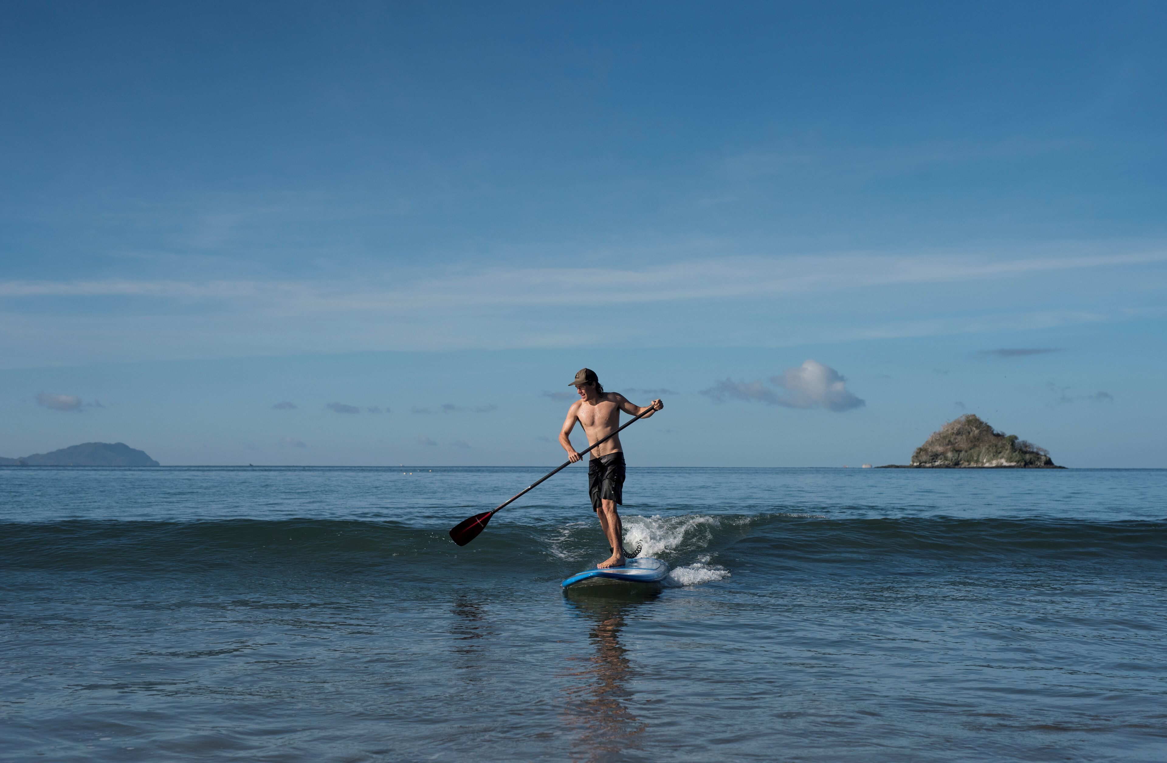 Una persona fa paddleboarding su acqua limpida, con un'isola in lontananza e cielo sereno.