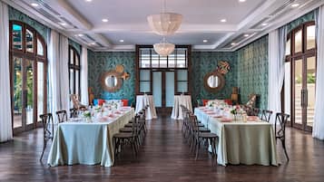 Een ruime eetruimte met lange tafels gedekt voor een maaltijd, grote ramen en decoratieve spiegelwanden.
