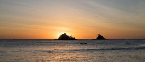A sunset over a calm sea with two islands silhouetted against the sky.