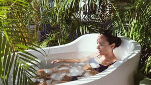 Une personne se détend dans une baignoire remplie de glace, entourée d’une végétation luxuriante.