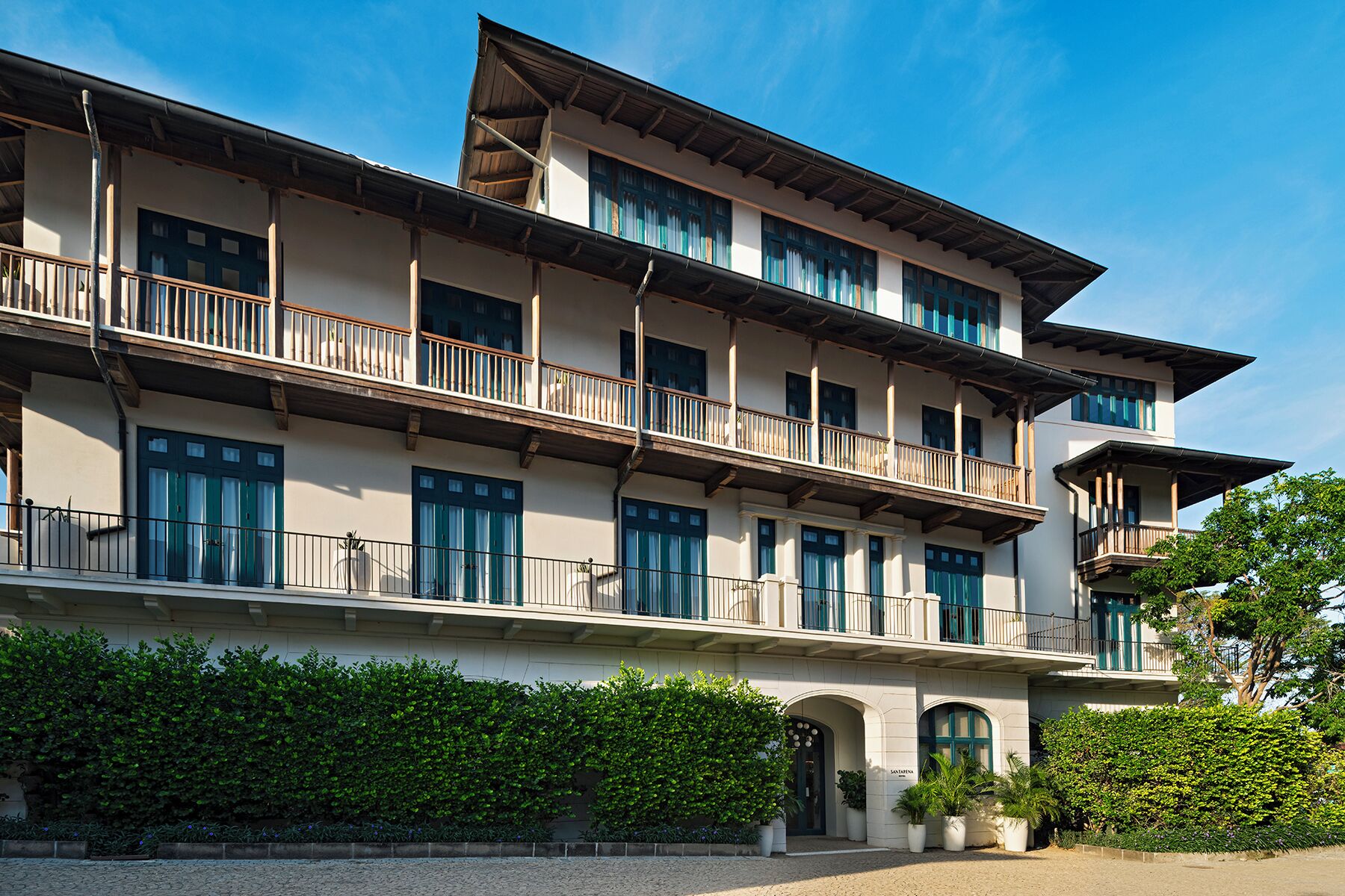 A multi-story hotel with a symmetrical facade, balconies, and a well-maintained hedge in front.