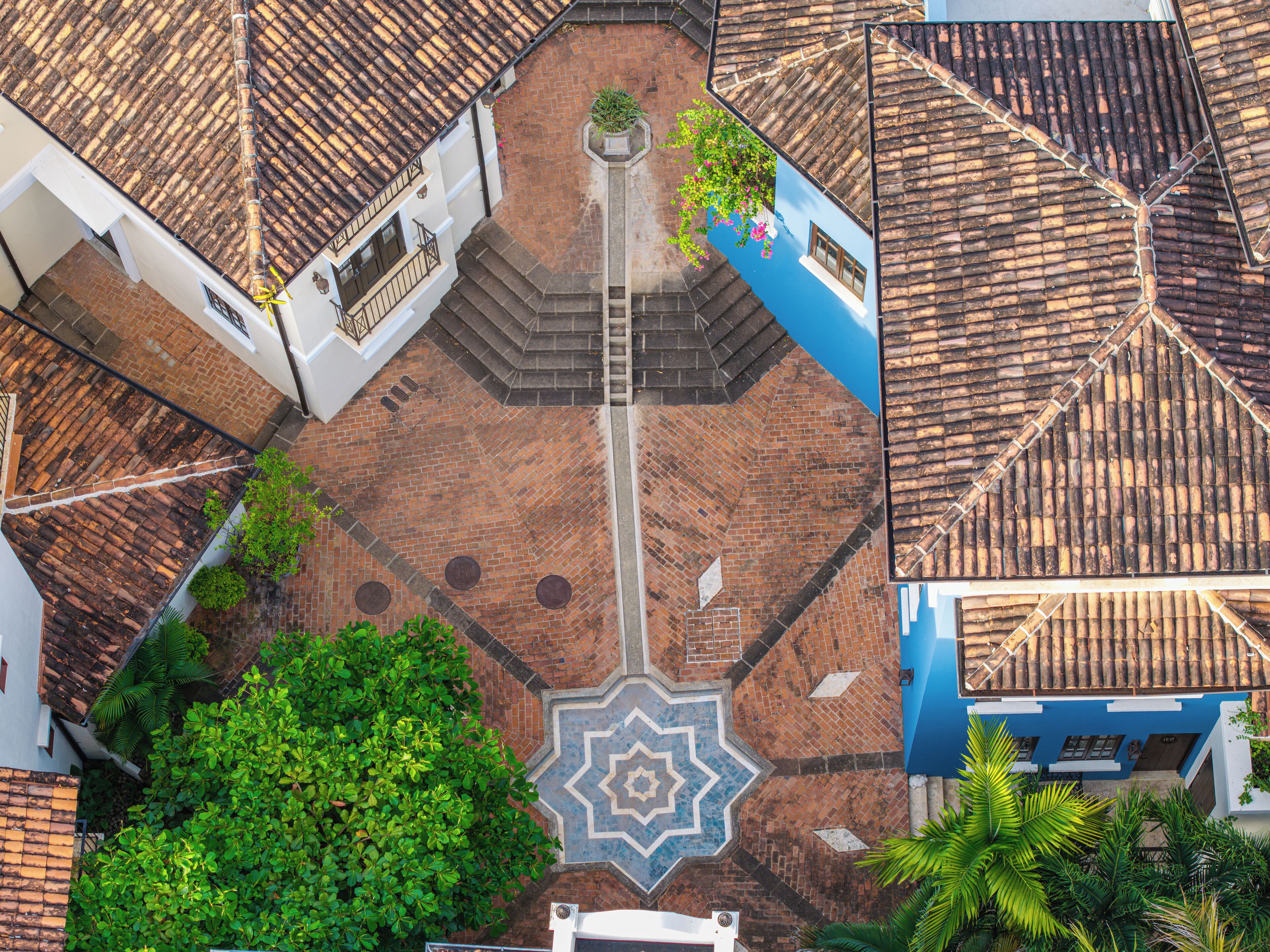 An aerial view of a courtyard with a central geometric tile pattern, surrounded by buildings with tiled roofs and brick walls.