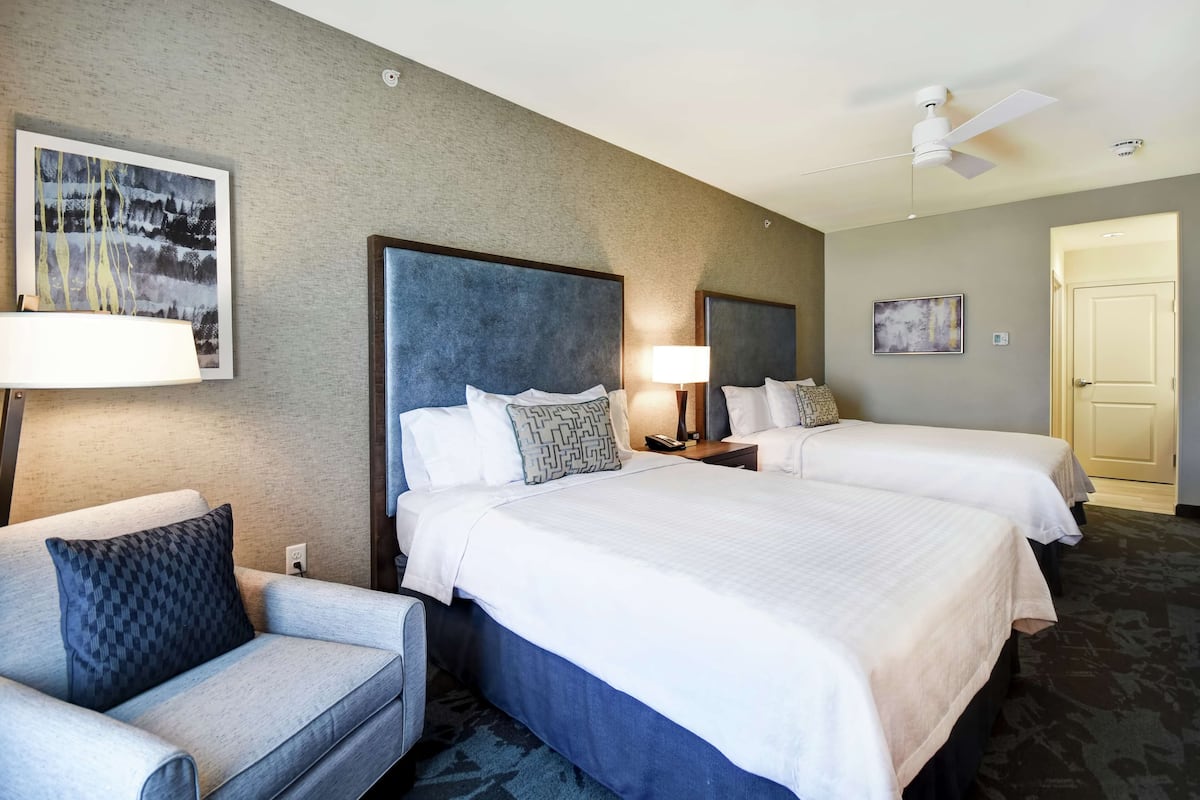 A hotel room with two beds, a sofa, a ceiling fan, and artwork on the walls.