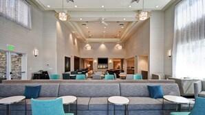A spacious lobby with a central seating area, multiple tables, and a large television screen. - Homewood Suites by Hilton Salt Lake City Airport (Salt Lake City)