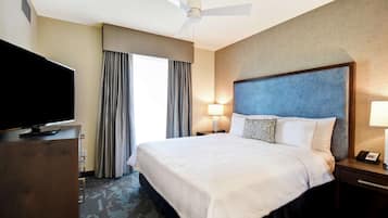 A hotel room with a large bed, a flat-screen TV, a ceiling fan, and a nightstand with a lamp.