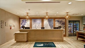 A hotel reception area with a wooden reception desk, a digital check-in kiosk, and a large mural on the wall. - Homewood Suites by Hilton Salt Lake City Airport (Salt Lake City)