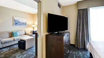 A hotel room with a flat-screen TV, a sofa, a desk, a dresser, and a bed.