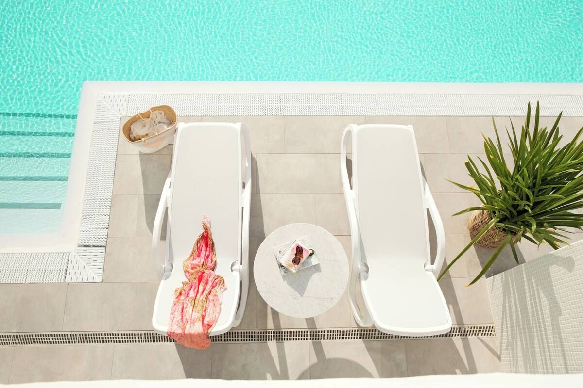 A poolside area with two white lounge chairs, a small round table, and a potted plant.