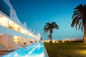 A hotel with a pool, palm trees, and a well-lit exterior at dusk. - Ocean Beach Club Gran Canaria (Mogan)
