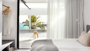 Un dormitorio moderno con cama, mesita de noche, perchero y vista al océano.