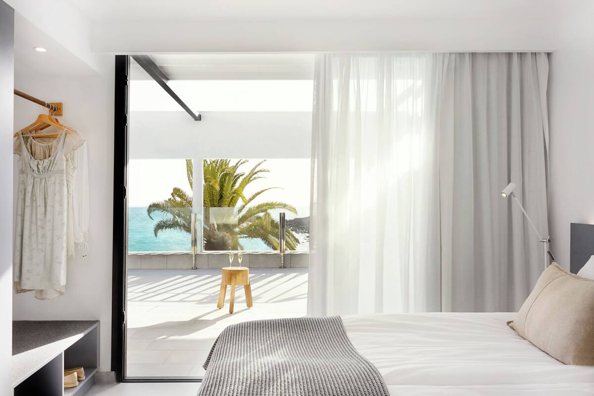 A modern bedroom with a bed, a nightstand, a hanging robe, and a view of the ocean.