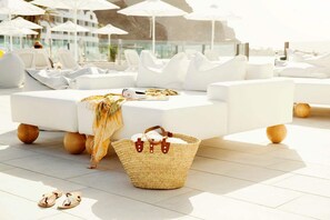 A sunlit outdoor seating area with white lounge chairs and a woven basket on the floor. - Ocean Beach Club Gran Canaria (Mogan)