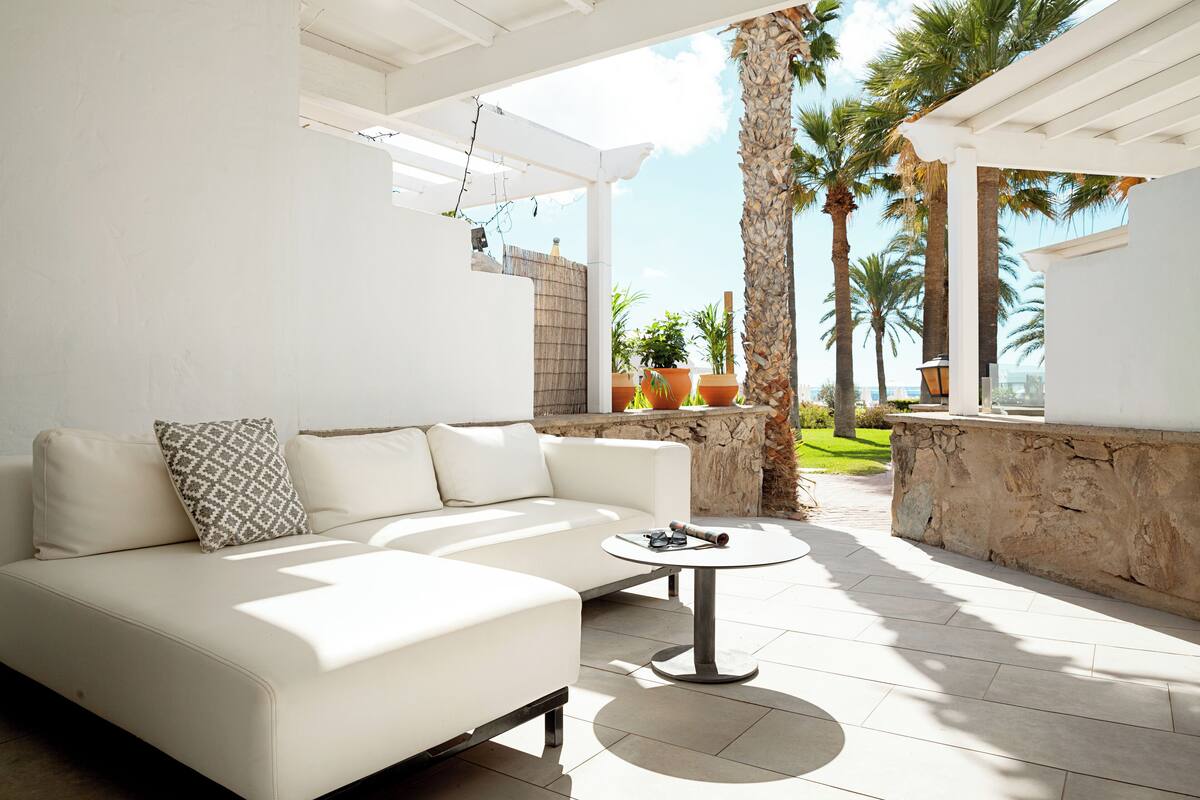 A modern outdoor living area with a white sofa, a round table, and a stone wall.