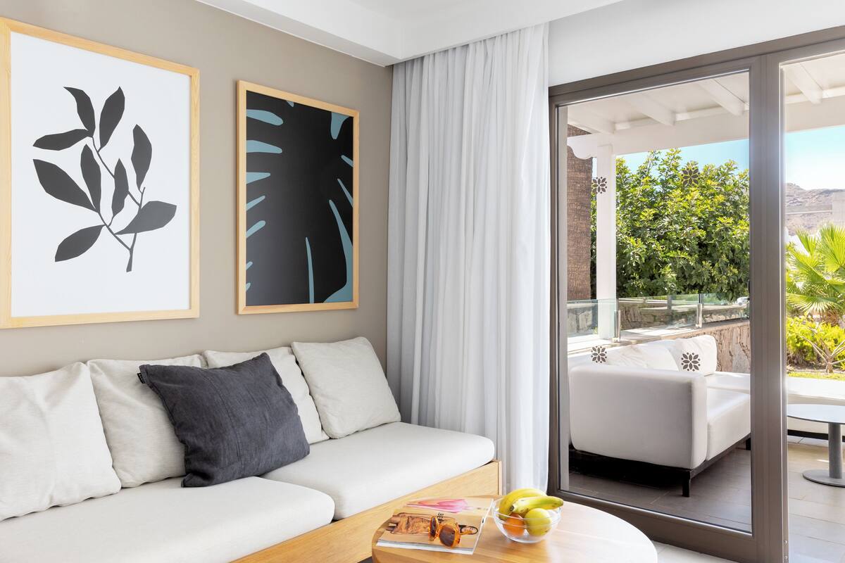 A modern living room with a sofa, a coffee table with magazines and fruit, and a balcony with outdoor furniture.