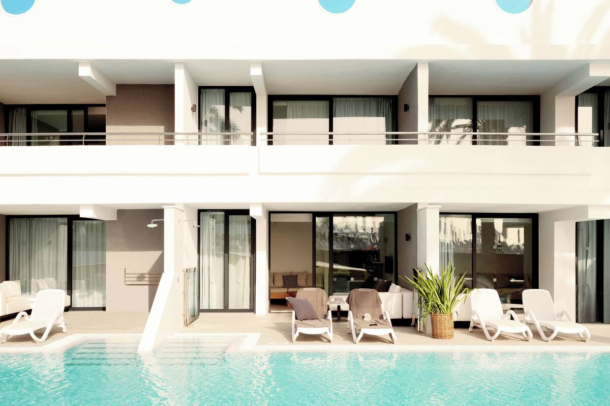 A modern hotel with a pool, lounge chairs, and a balcony with a view.