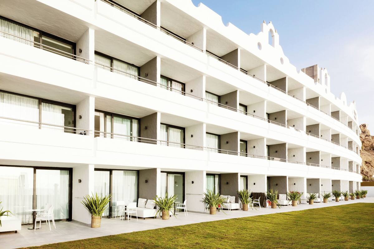 A multi-story hotel with balconies, outdoor seating, and a well-maintained lawn.