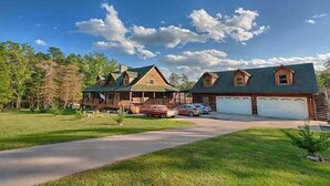 Une grande cabane en rondins dotée d’un porche couvert, d’un garage et d’une allée.
