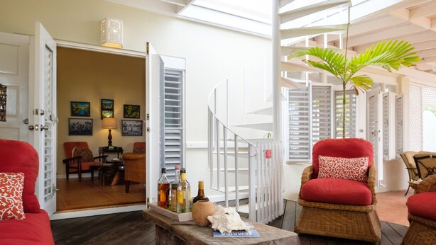 A cozy indoor space with a wooden floor, red and wicker furniture, a staircase, and a view of a dining area. - Dreamin Villa  Villa 4 (Duncans)