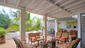 A covered outdoor seating area with cushioned chairs and tables, surrounded by potted plants and palm trees. - Dreamin Villa  Villa 4 (Duncans)