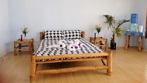 Una cama con estampado pata de gallo, cabecera y piecera de madera, flanqueadas por dos mesitas de noche con jarrones de flores.