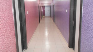 Un pasillo con paredes rosadas y moradas, puertas a ambos lados y piso de baldosas.