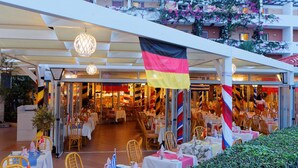 Un'area pranzo all'aperto con tavoli e sedie, una bandiera e un edificio sullo sfondo.